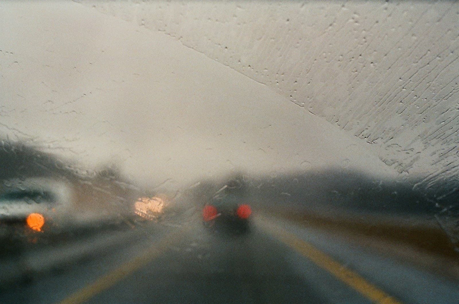 Heavy raindrops on a windshield with blurred vehicle lights on a wet highway ahead